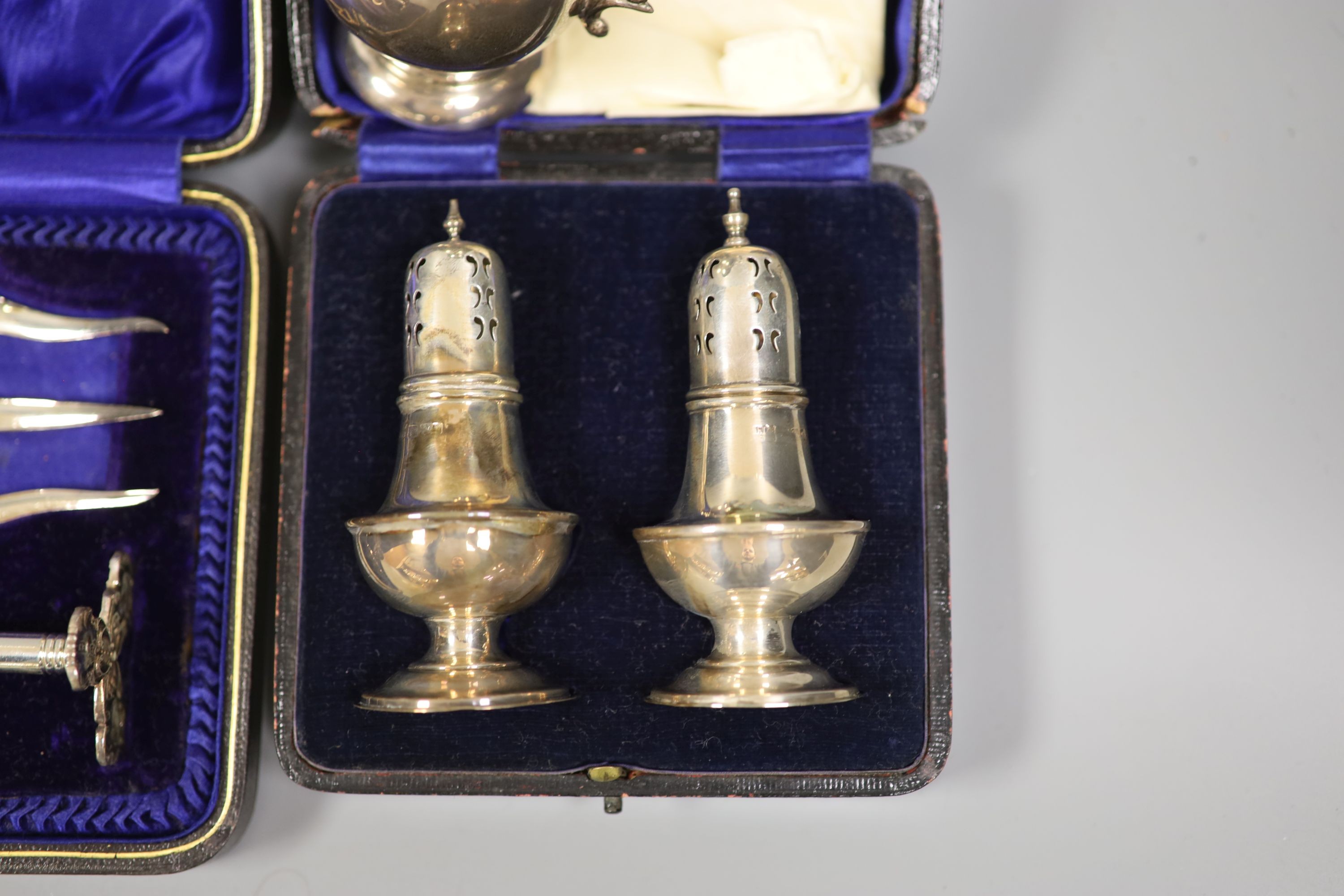 A 1920's silver small mug, a cased pair of silver pepperettes and a cased pair of knife rests and fork.